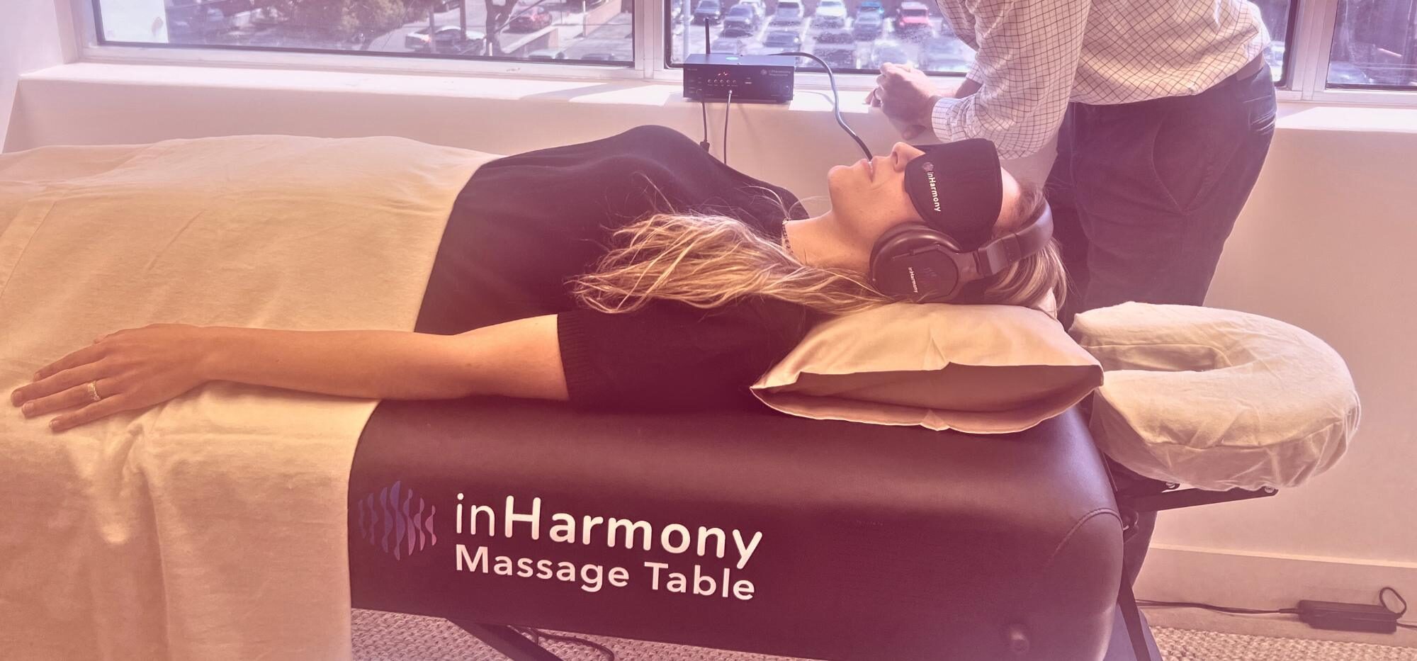 Soundbed therapy session with a practitioner adjusting controls as a woman relaxes on an inHarmony table wearing headphones.