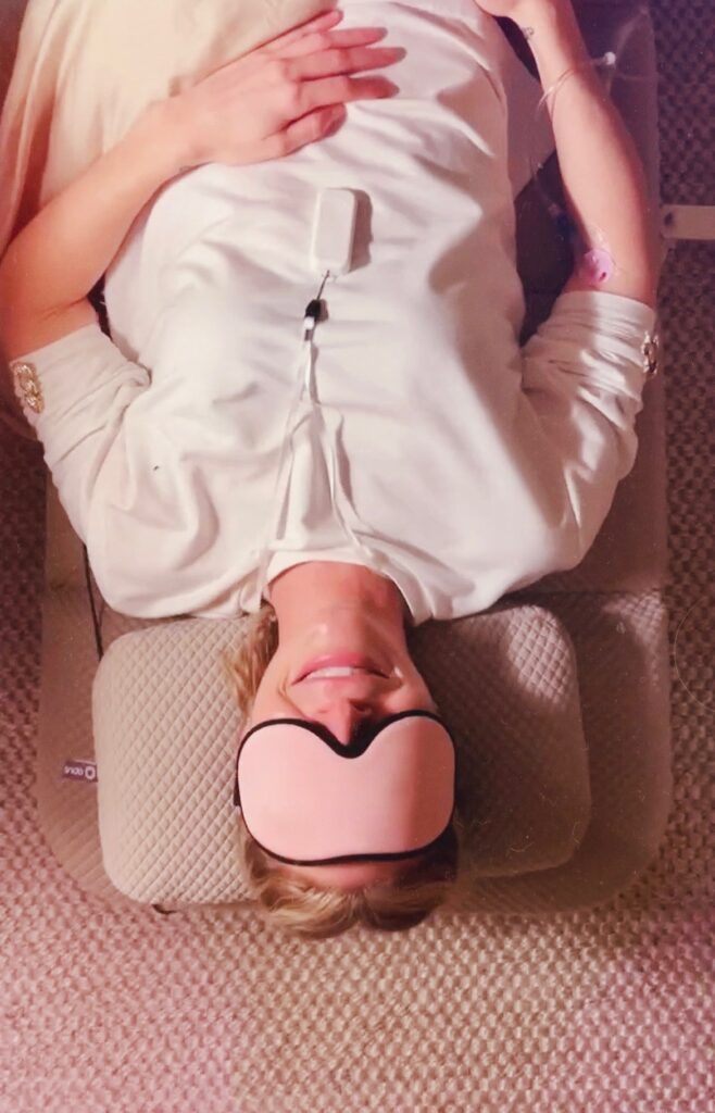 Soundbed therapy experience with a woman lying on a mat wearing an eye mask and IV drip in a peaceful setting.