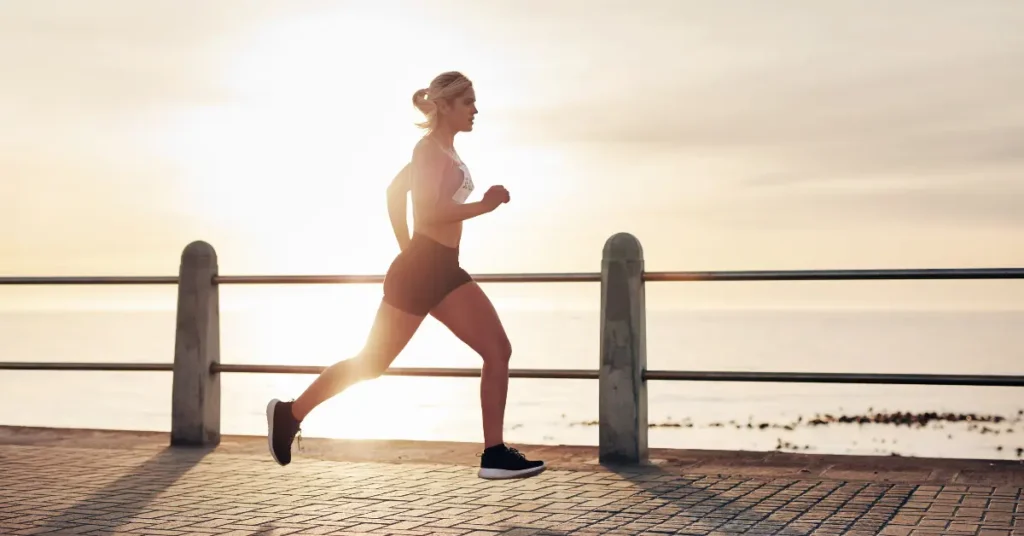 IV hydration for athletes helps support energy and recovery, shown by a woman running along the ocean at sunrise.