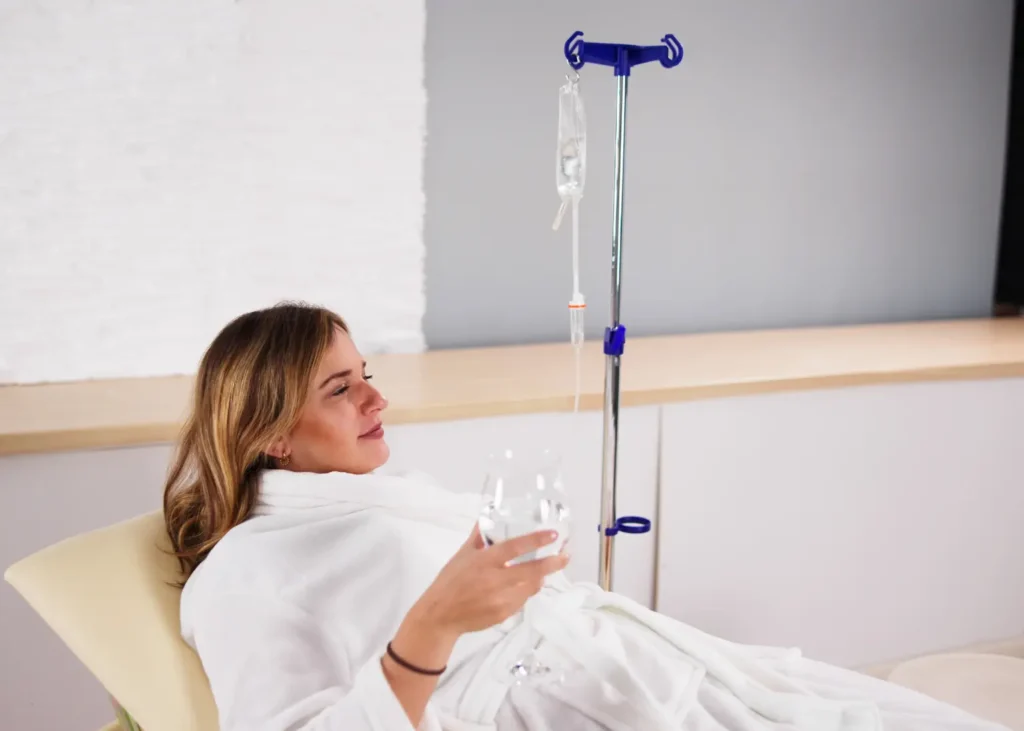 IV hydration drip treatment with a woman lounging in a robe while holding a glass of water