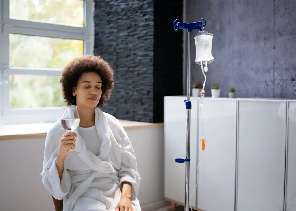 Anxiety and depression therapy session with a woman in a robe receiving IV treatment while holding a water glass.