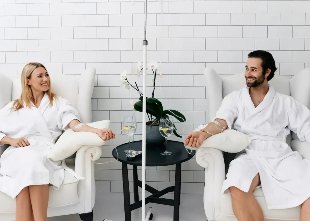 Ketamine-assisted therapy session with a smiling couple receiving IV drips in a relaxing spa setting.