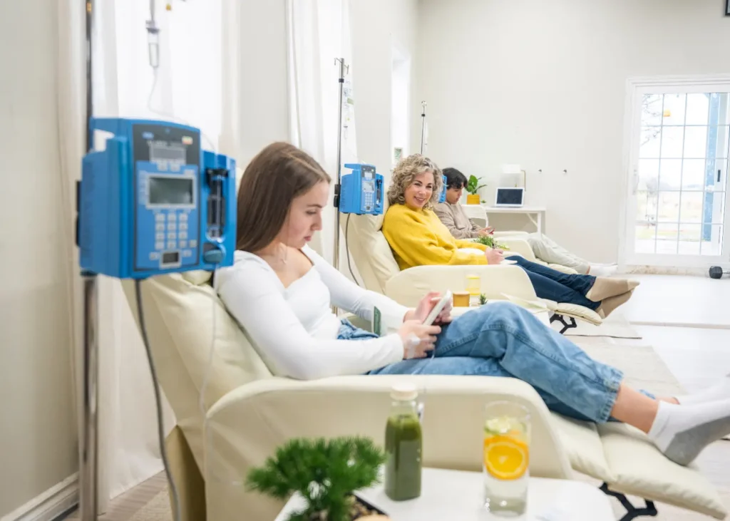 Ketamine treatment session with three relaxed individuals receiving IV infusions in a bright clinic lounge.