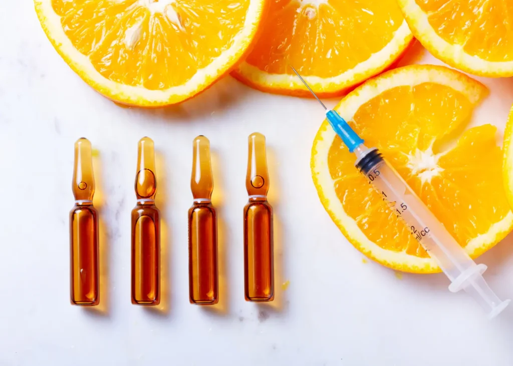 Vitamin C infusion concept with ampoules, syringe, and fresh orange slices on a white background