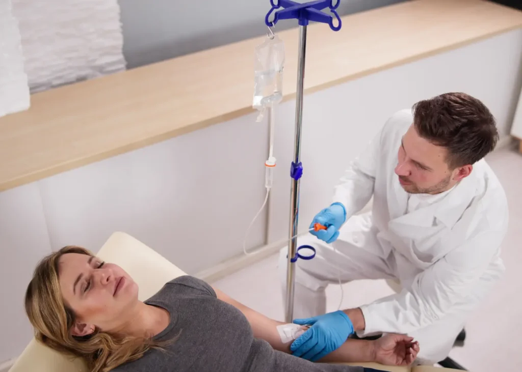 Healthcare provider administering IV vitamin therapy to a woman reclining during treatment.