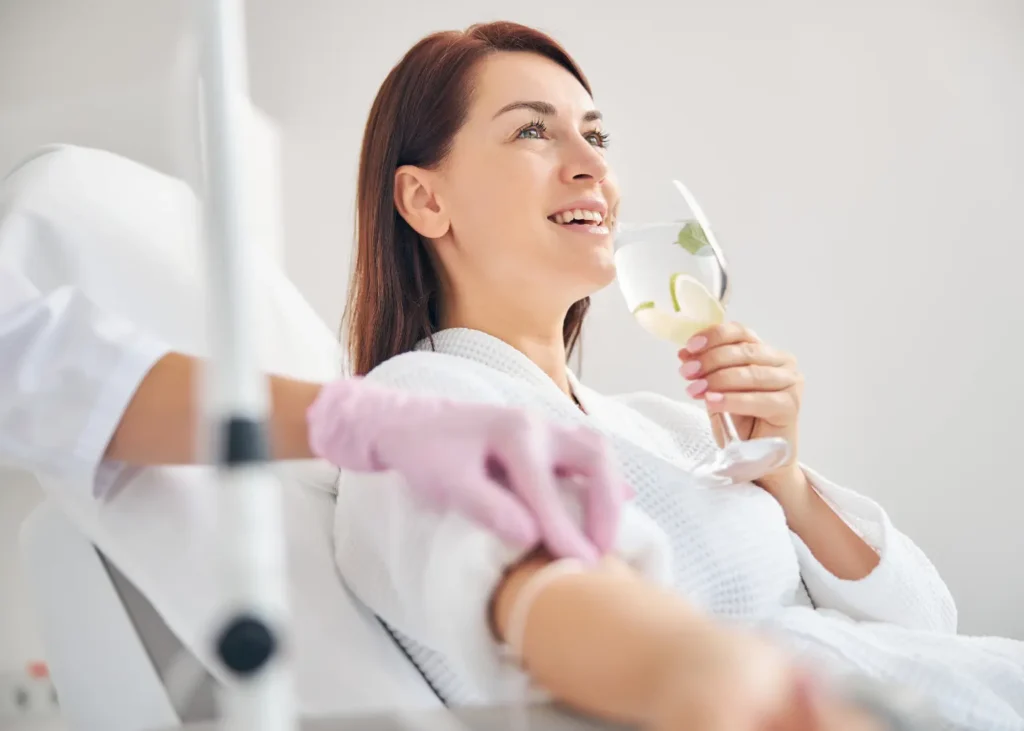 Depression treatment represented by a smiling woman receiving IV therapy while sipping citrus-infused water.