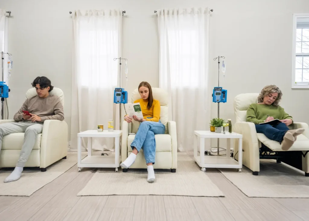 Group of people seated in recliners receiving vitamin infusion therapy with IV drips in a wellness clinic.
