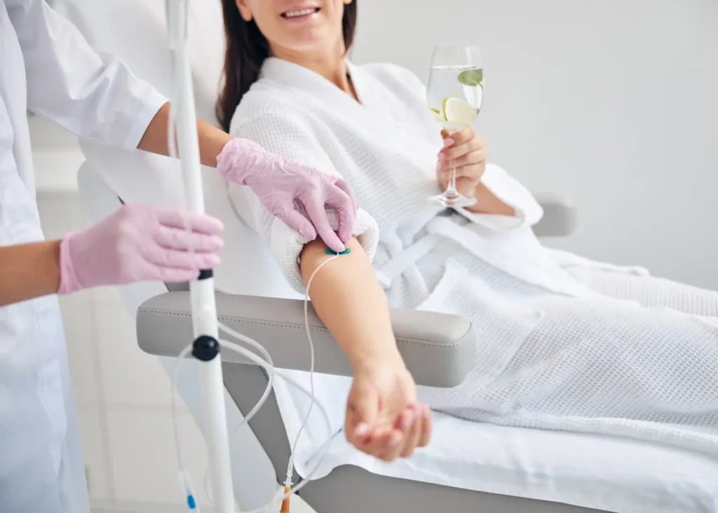 IV depression treatment with a smiling woman holding citrus water while receiving an intravenous infusion.