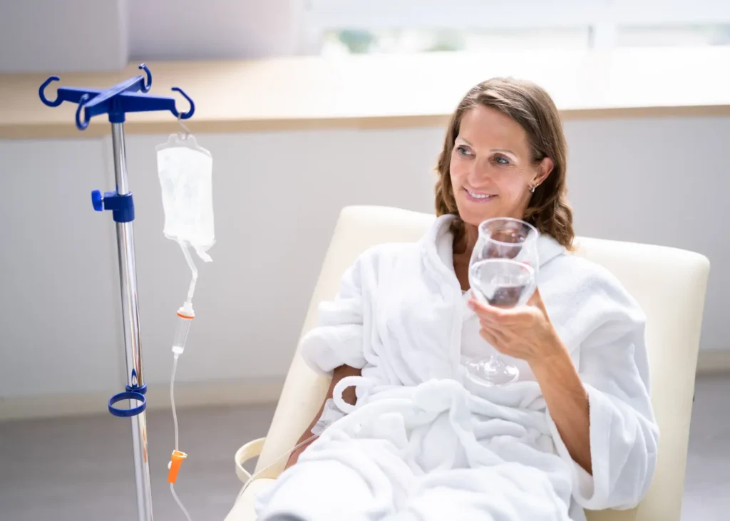 NAD+ treatment with a smiling woman in a robe receiving IV infusion while holding a glass of water.