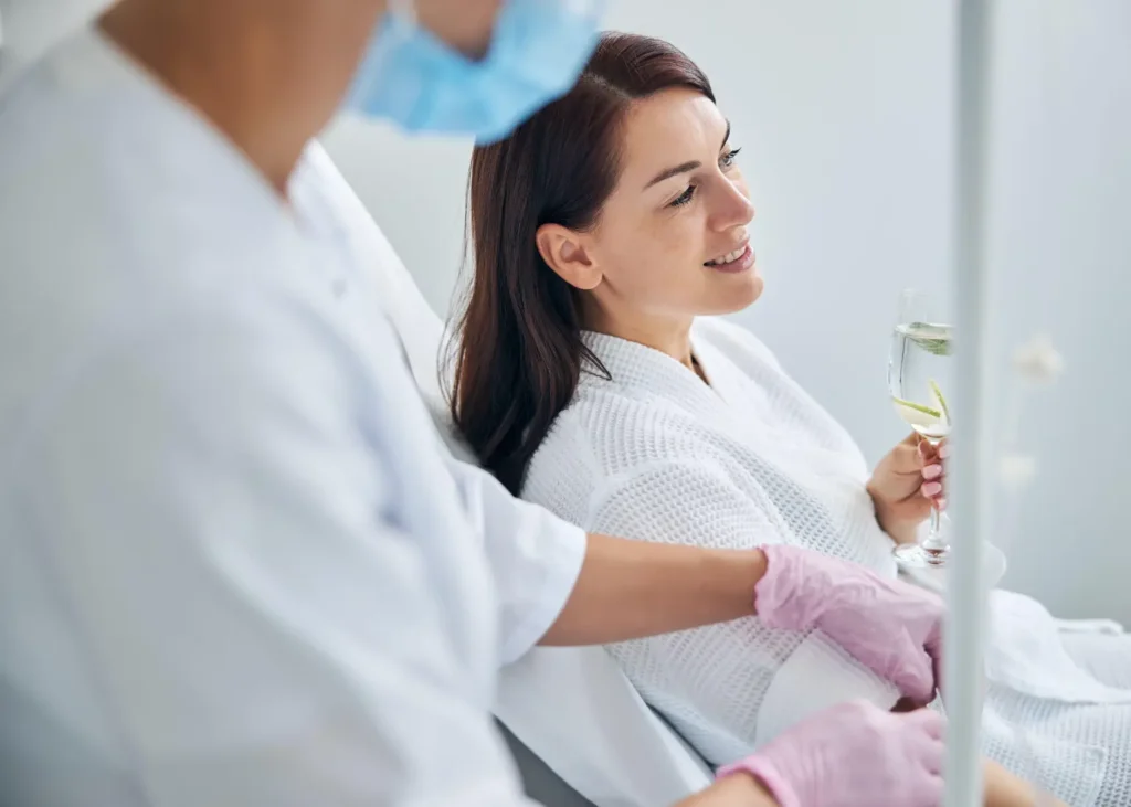 Anxiety treatment infusions with a smiling woman holding citrus water while a nurse manages her IV drip.