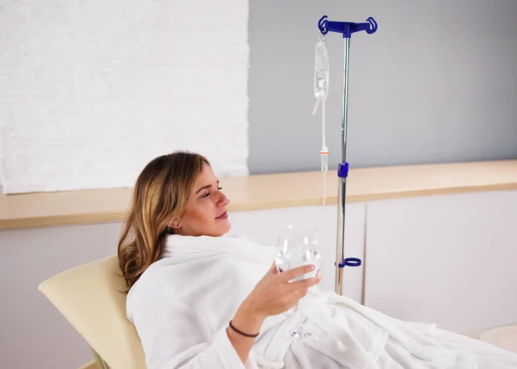 Wellness IV drips shown with a relaxed woman in a spa-like chair holding water during treatment.